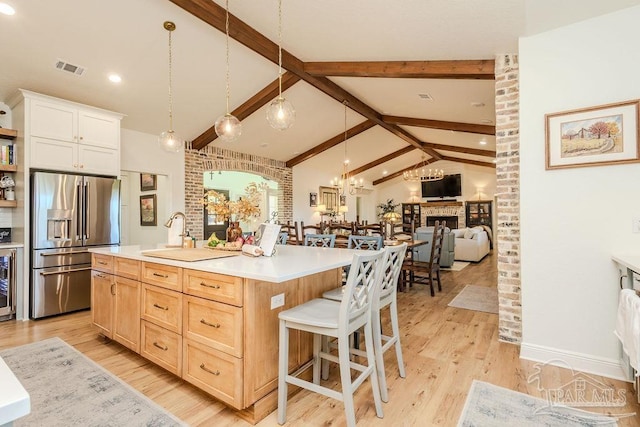 kitchen with stainless steel fridge with ice dispenser, lofted ceiling with beams, light brown cabinetry, a sink, and a kitchen breakfast bar