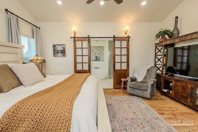 bedroom with recessed lighting, wood finished floors, ensuite bath, and a barn door