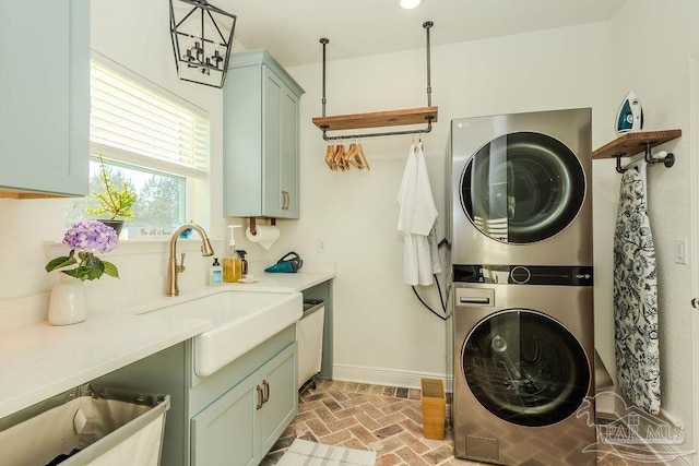 laundry room featuring brick floor, stacked washer and dryer, a sink, baseboards, and cabinet space