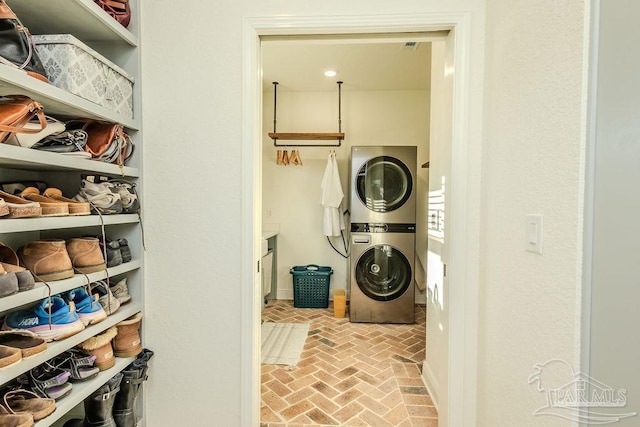 clothes washing area featuring laundry area, brick floor, and stacked washer / dryer