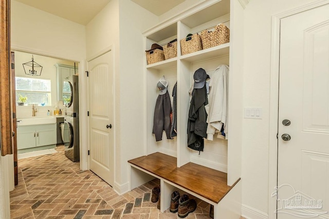 mudroom with brick floor, a sink, and stacked washer and clothes dryer