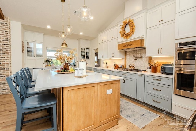 kitchen with lofted ceiling, light wood-style flooring, stainless steel appliances, light countertops, and backsplash