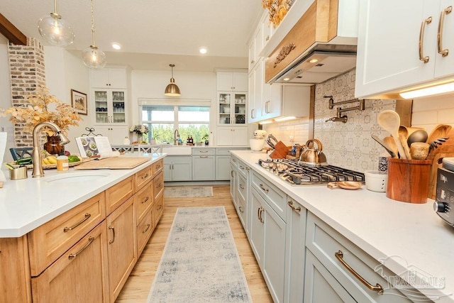 kitchen featuring a sink, custom exhaust hood, glass insert cabinets, and stainless steel gas stovetop