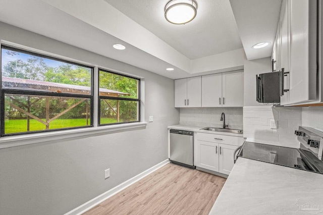4905 State St, Pensacola, FL 32506 - kitchen with appliances with stainless steel finishes, a sink, white cabinets, backsplash, and light wood-type flooring