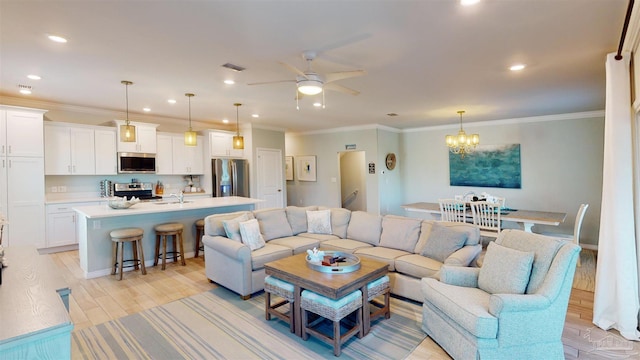 living room with ceiling fan with notable chandelier, light wood-type flooring, ornamental molding, and sink