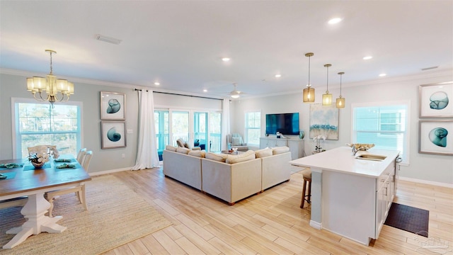 living room featuring ceiling fan with notable chandelier, light hardwood / wood-style floors, crown molding, and sink