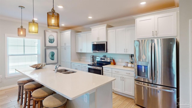 kitchen featuring stainless steel appliances, a kitchen island with sink, sink, pendant lighting, and white cabinets