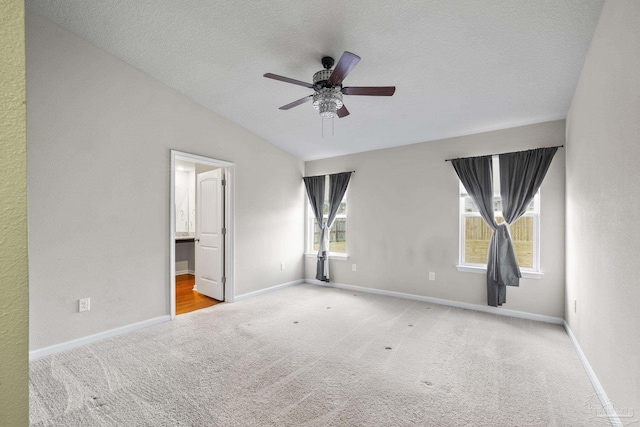 unfurnished bedroom with ensuite bath, lofted ceiling, light colored carpet, ceiling fan, and a textured ceiling