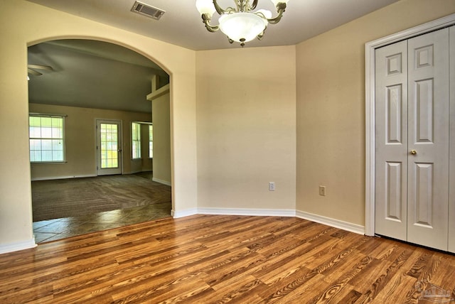 interior space with arched walkways, visible vents, wood finished floors, a chandelier, and baseboards