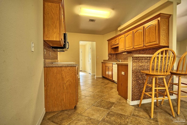 kitchen featuring a kitchen bar, white dishwasher, dark tile patterned flooring, and backsplash