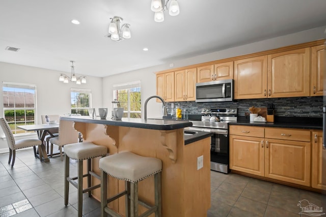 kitchen featuring pendant lighting, an inviting chandelier, a center island with sink, decorative backsplash, and appliances with stainless steel finishes