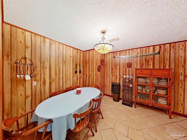 dining area with a textured ceiling, a notable chandelier, and wood walls