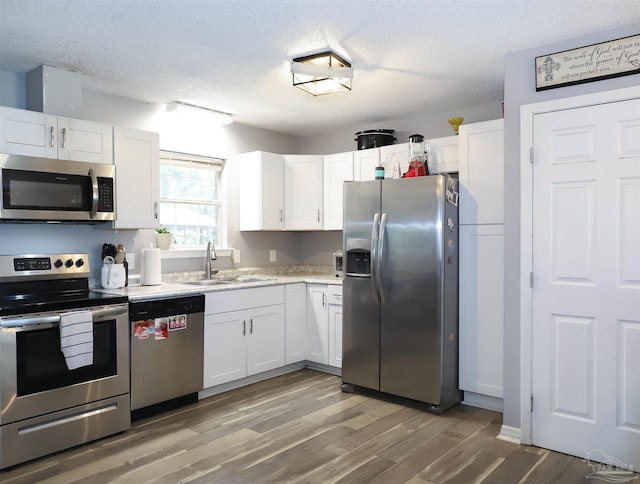 kitchen with hardwood / wood-style floors, appliances with stainless steel finishes, white cabinetry, and sink