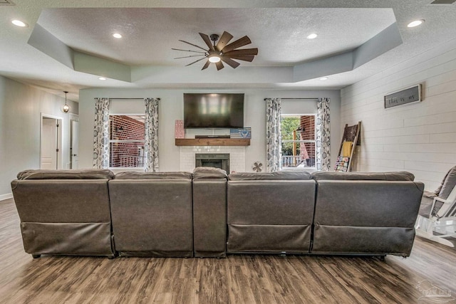 living room with a textured ceiling, a raised ceiling, ceiling fan, wooden walls, and hardwood / wood-style flooring