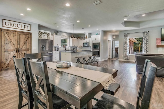 dining space featuring a barn door, sink, light wood-type flooring, and a textured ceiling