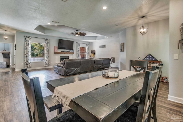 dining space featuring a raised ceiling, ceiling fan, a fireplace, and hardwood / wood-style floors