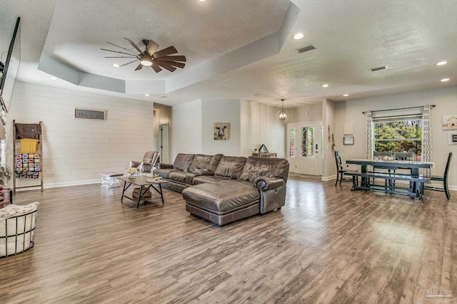 living room with a raised ceiling, ceiling fan, wood-type flooring, and a textured ceiling