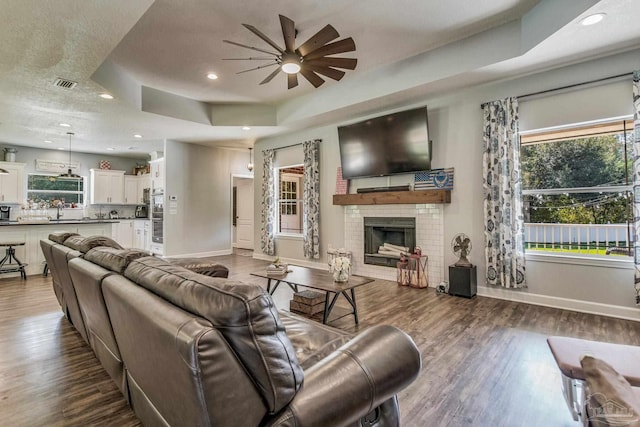 living room featuring a raised ceiling, ceiling fan, sink, a fireplace, and dark hardwood / wood-style floors