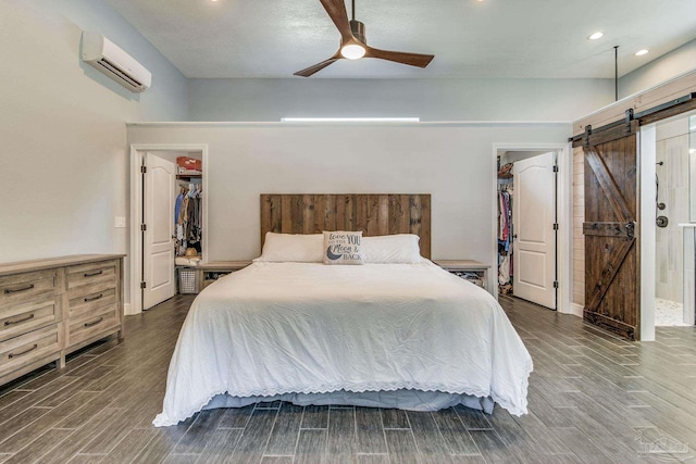 bedroom with an AC wall unit, ceiling fan, a barn door, a spacious closet, and a closet