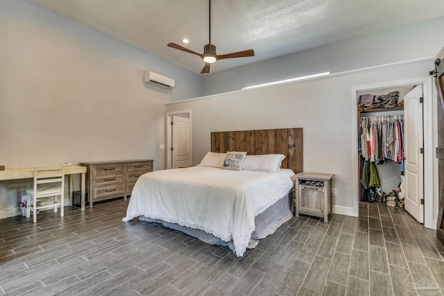 bedroom with a wall unit AC, ceiling fan, a barn door, hardwood / wood-style flooring, and a closet