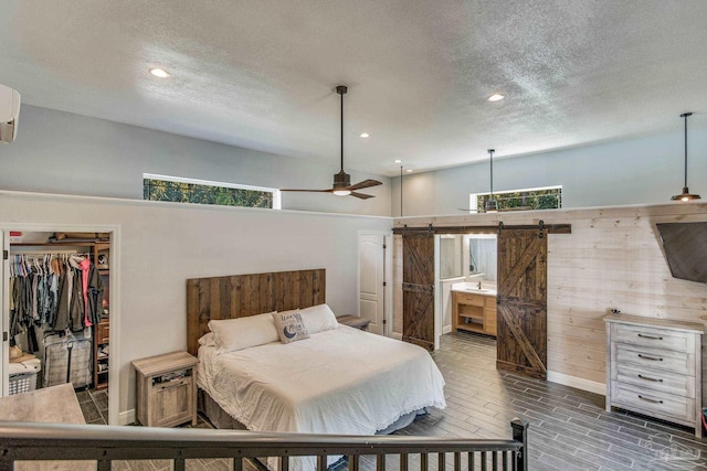 bedroom featuring ensuite bath, ceiling fan, a barn door, dark hardwood / wood-style floors, and a closet