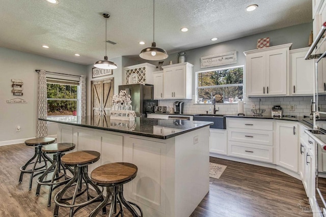 kitchen with sink, decorative light fixtures, white cabinets, a kitchen island, and stainless steel refrigerator