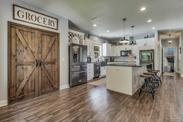 kitchen with a center island, a textured ceiling, decorative light fixtures, white cabinetry, and stainless steel appliances