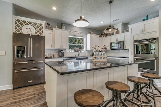 kitchen featuring appliances with stainless steel finishes, a textured ceiling, pendant lighting, white cabinets, and a center island