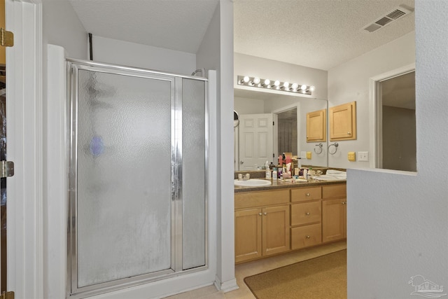 bathroom with tile patterned flooring, vanity, a shower with shower door, and a textured ceiling