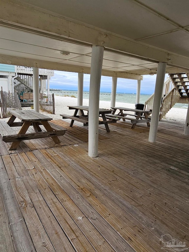 wooden terrace featuring a beach view and a water view