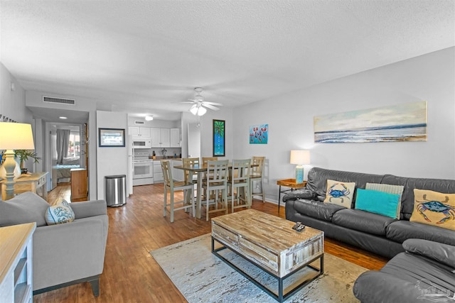 living room with ceiling fan, a textured ceiling, and light wood-type flooring