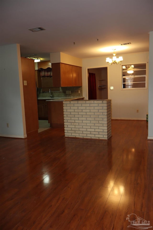 kitchen featuring sink, kitchen peninsula, backsplash, dark wood-type flooring, and a notable chandelier