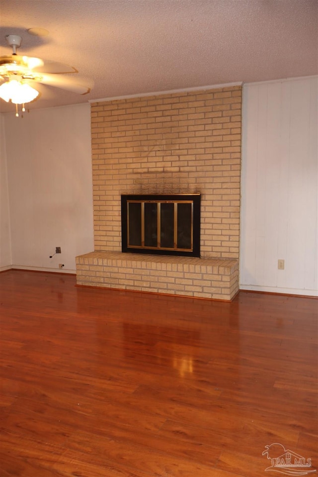 unfurnished living room with ceiling fan, a brick fireplace, hardwood / wood-style floors, and a textured ceiling