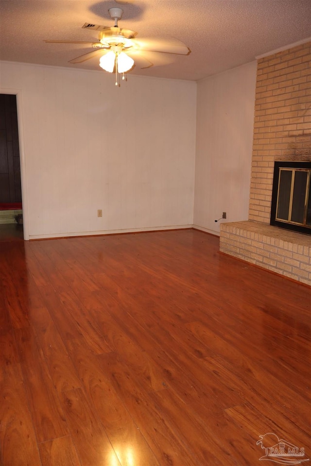 unfurnished living room with hardwood / wood-style floors, a textured ceiling, a brick fireplace, brick wall, and ceiling fan