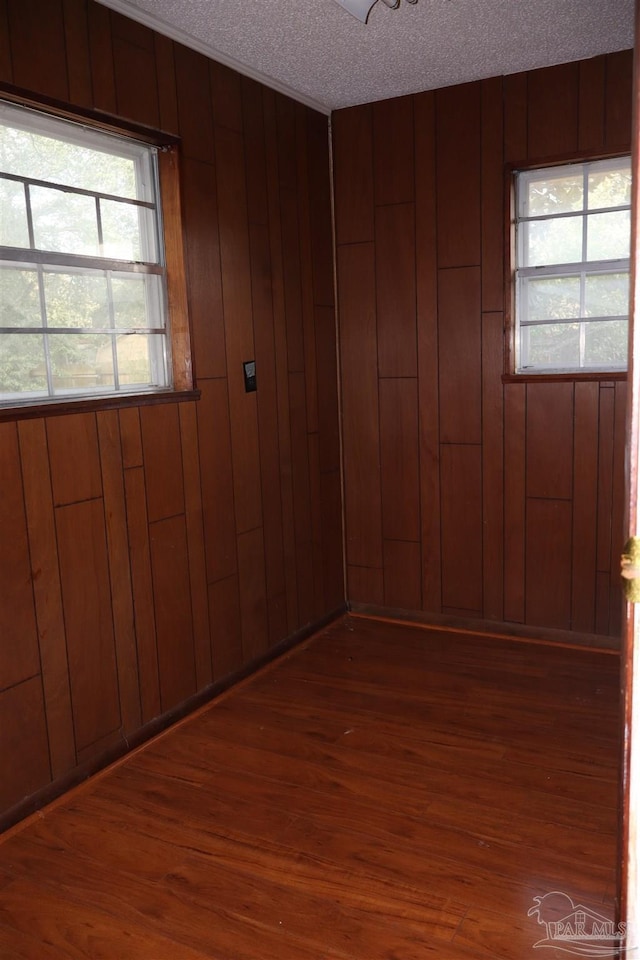 empty room with dark wood-type flooring, a textured ceiling, and wood walls