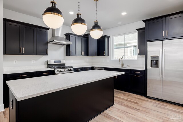 kitchen with stainless steel appliances, hanging light fixtures, wall chimney exhaust hood, sink, and light hardwood / wood-style floors