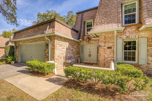 view of front of house featuring mansard roof, an attached garage, brick siding, a shingled roof, and driveway