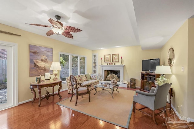 living room featuring a ceiling fan, a fireplace with raised hearth, baseboards, and wood finished floors