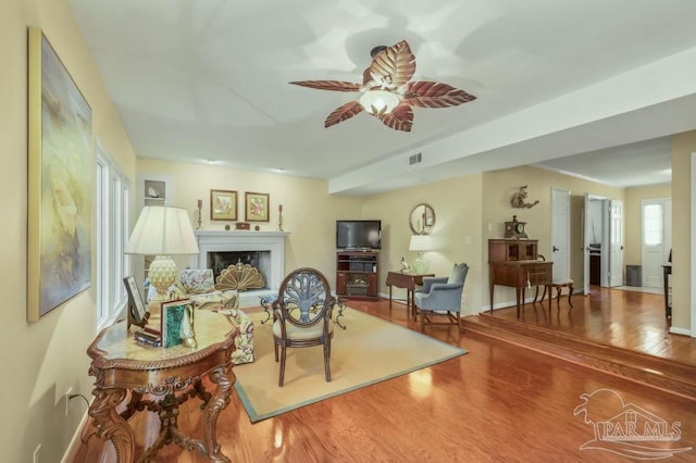 living area featuring a fireplace, wood finished floors, a ceiling fan, and baseboards