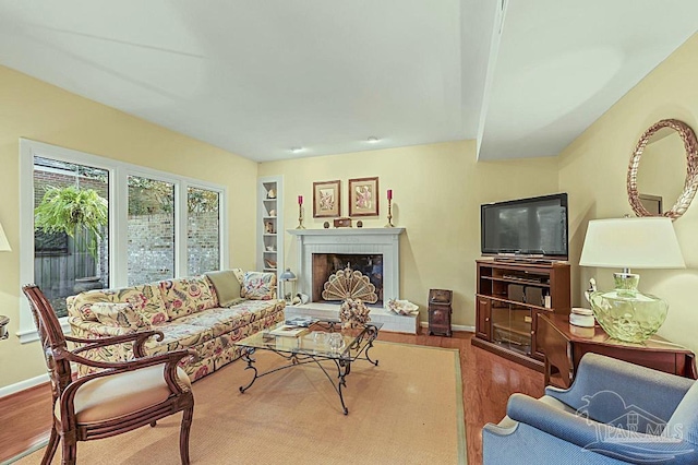 living room with a fireplace with raised hearth, wood finished floors, and baseboards