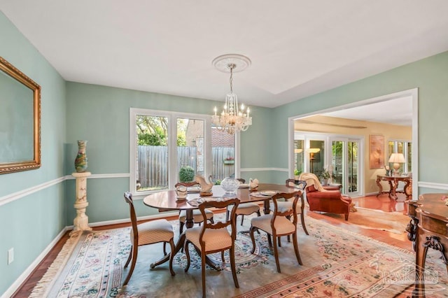 dining area with a wealth of natural light, baseboards, wood finished floors, and an inviting chandelier