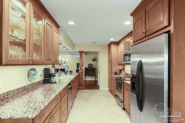 kitchen featuring stainless steel appliances, brown cabinetry, a sink, and light stone counters