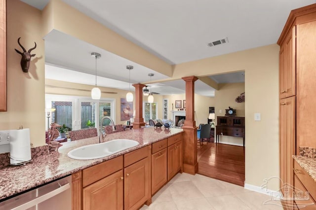 kitchen featuring a sink, visible vents, stainless steel dishwasher, light stone countertops, and decorative columns