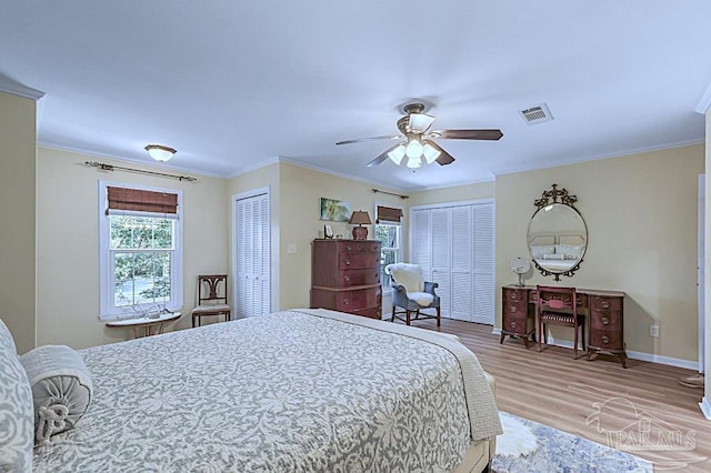 bedroom with wood finished floors, visible vents, crown molding, and two closets