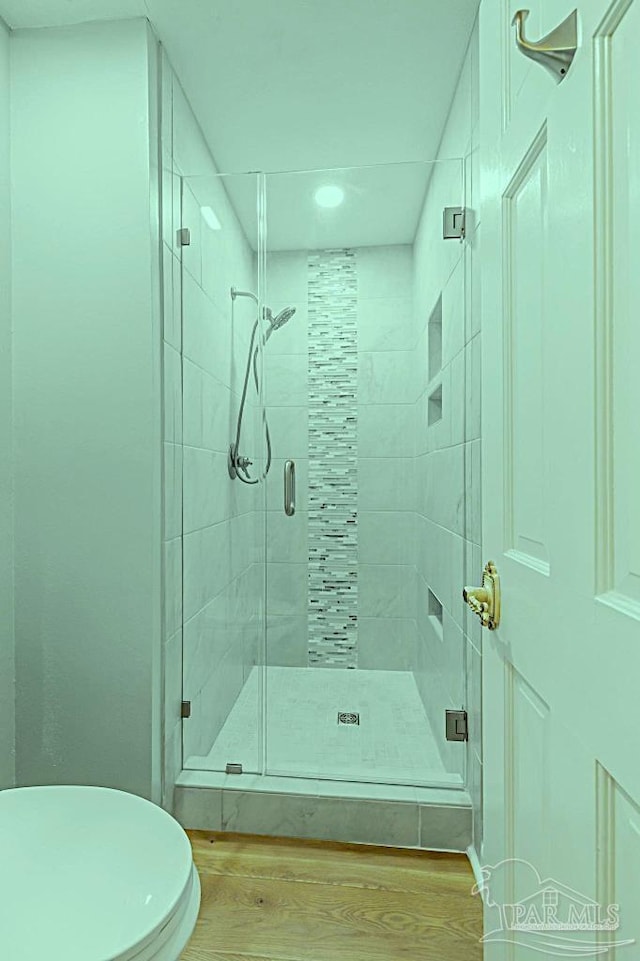 bathroom featuring a shower stall, toilet, and wood finished floors