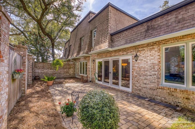 back of property with brick siding, a patio area, mansard roof, and roof with shingles