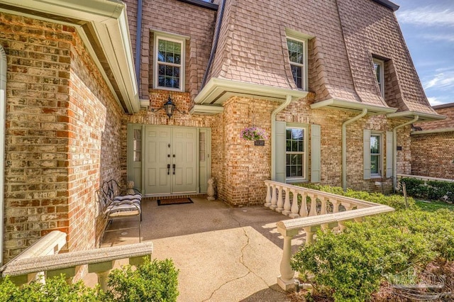 entrance to property with roof with shingles, mansard roof, and brick siding