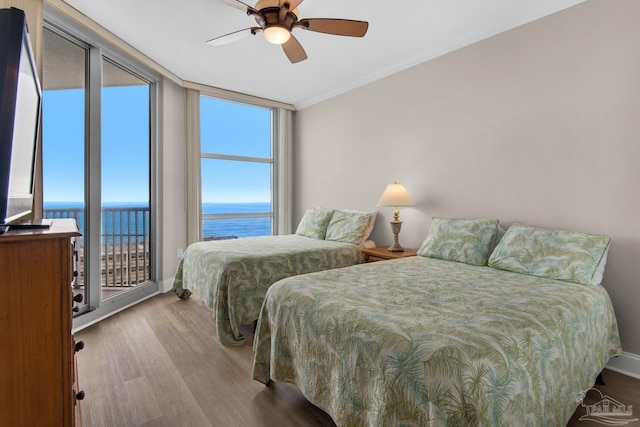 bedroom with a water view, light hardwood / wood-style flooring, ceiling fan, ornamental molding, and a wall of windows