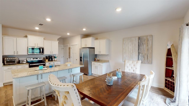 kitchen with a center island with sink, stainless steel appliances, and white cabinetry