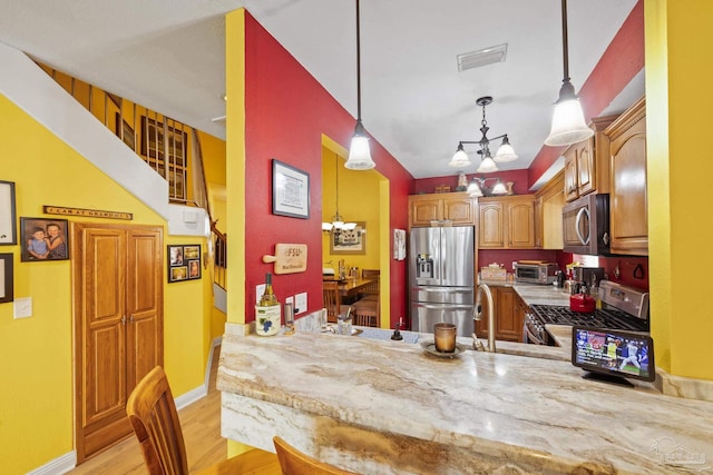 kitchen with appliances with stainless steel finishes, decorative light fixtures, a notable chandelier, kitchen peninsula, and light wood-type flooring